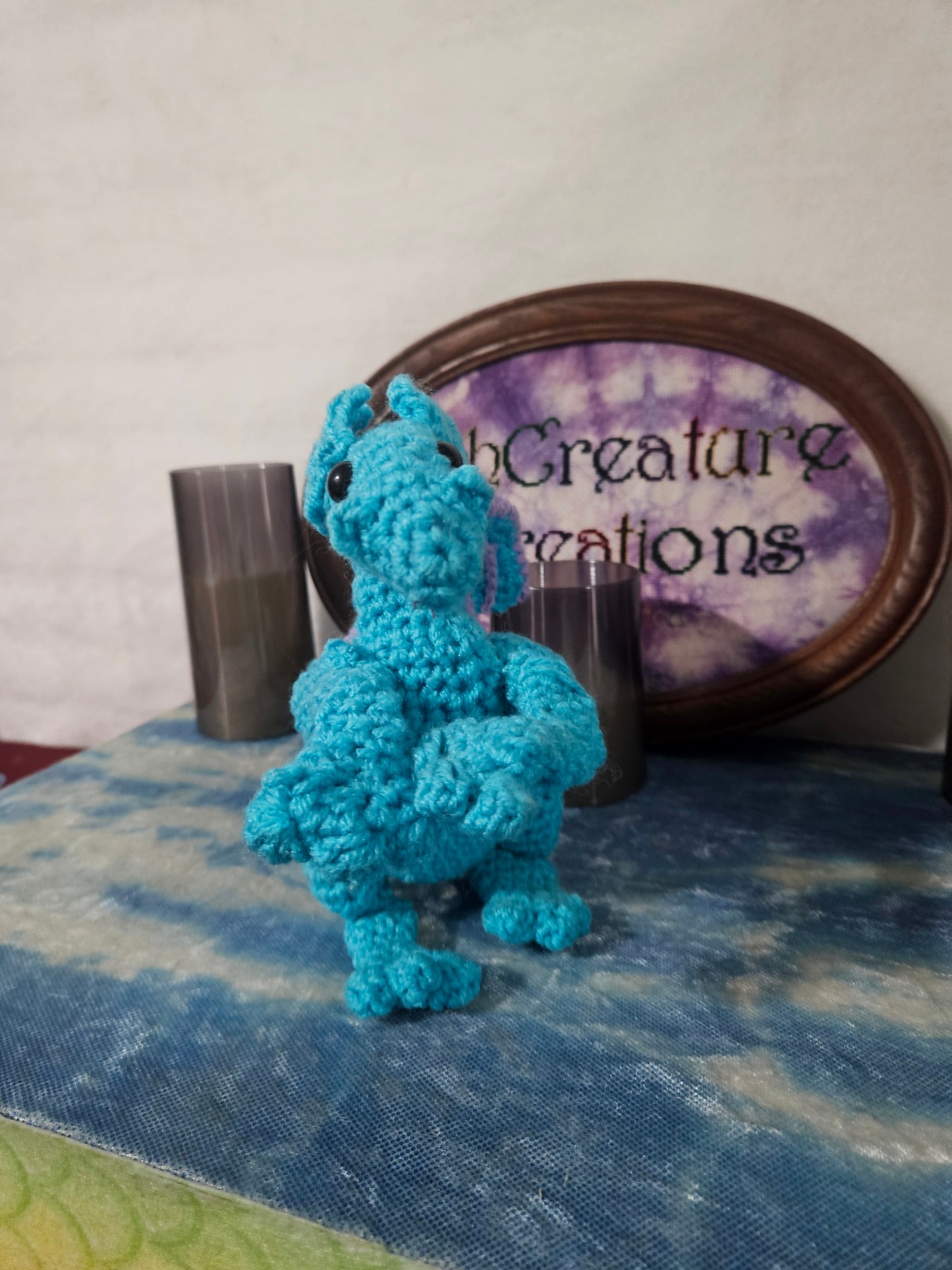Blue crocheted dragon toy on a textured surface with a blurred background