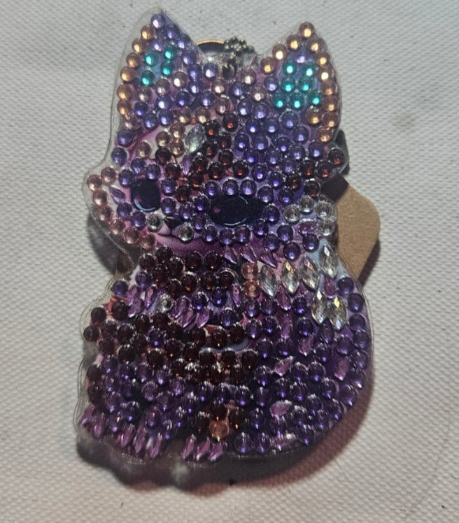 Purple beaded cat-shaped brooch on a textured fabric background