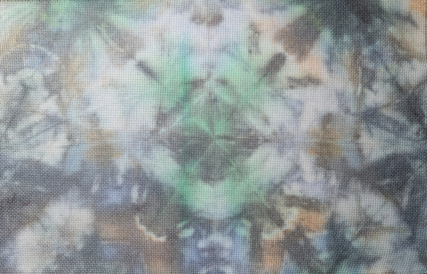 A rectangular woven fabric panel with an abstract tie-dye style pattern in shades of blue, green, beige, and gray, laid flat on a patterned beige surface.
