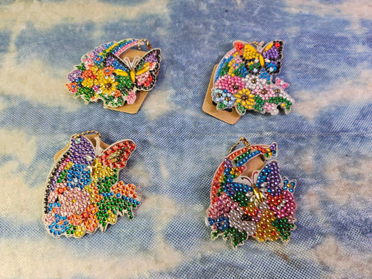 Four colorful butterfly-shaped pins on a textured blue fabric background