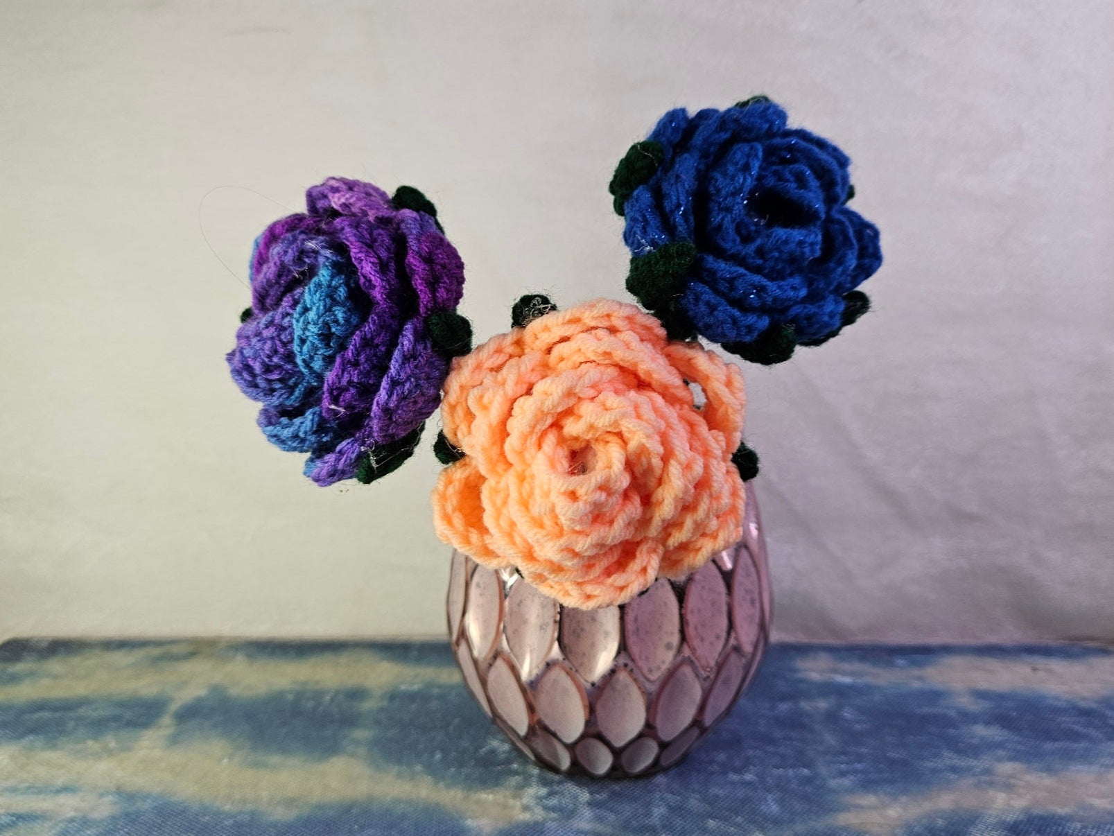 Decorative vase with crocheted flowers on a textured surface
