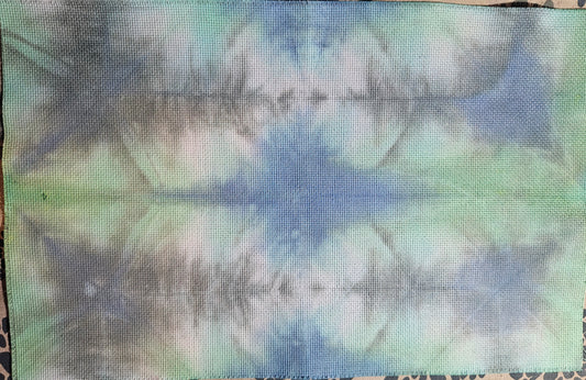 A rectangular piece of fabric with a blue, green, and white tie-dye pattern, laid flat on a patterned surface.