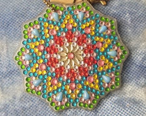 Decorative brooch with a colorful pattern on a cardboard backing, placed on a textured fabric surface.